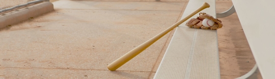 Baseball bat leaning on a single set of bleachers with a baseball glove with a baseball on it sitting on the bench
